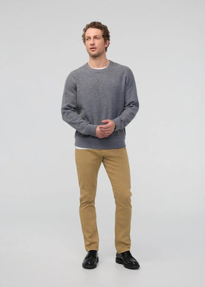 A man with short dark hair and a trimmed beard stands against a white background, wearing a white t-shirt, white sneakers with black details, and DUER's DU/ER NO SWEAT RELAXED TAPER PANT in an athletic fit. One hand is in his pocket.