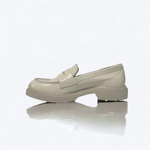 A single ANNA Loafer in Butter by MICHELE LOPRIORE, made with beige patent leather and featuring a chunky rubber sole, is displayed against a white background. This classic shoe showcases subtle stitched details and boasts a 3 cm height for added style.