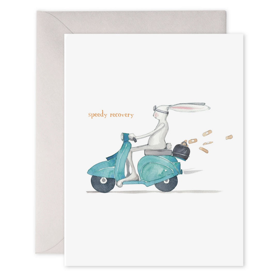 The E. FRANCES PAPER "Speedy Recovery" card features a rabbit in goggles on a teal scooter, leaving behind carrots, with "speedy recovery" printed in orange on luxe heavyweight paper. Adds charm to any wish!.