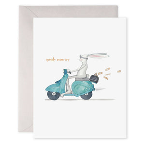 The E. FRANCES PAPER "Speedy Recovery" card features a rabbit in goggles on a teal scooter, leaving behind carrots, with "speedy recovery" printed in orange on luxe heavyweight paper. Adds charm to any wish!.