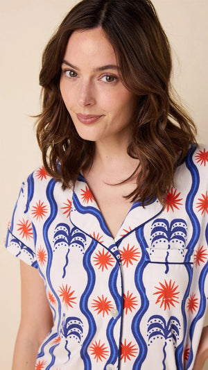 A person in CAT'S PAJAMAS - RED, WHITE AND BREEZE PIMA PAJAMA SHORT SET from CAT'S PAJAMAS stands barefoot sideways on a beige background, glancing back over their shoulder.