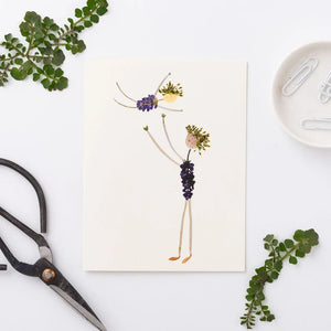 The PETAL PEOPLE PRESS Father's Day card shows a whimsical illustration on FSC-certified cardstock with two figures made of pressed flowers and leaves. The taller figure lifts the smaller one, both featuring leafy limbs and bodies adorned with vibrant purple flowers.