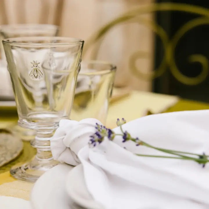 The LA ROCHERE BEE WATER GLASS, with its embossed Napoleonic bee, rests on a sunlit table beside a green lime drink, fresh cantaloupe slices, and white flowers for an effortlessly elegant display.