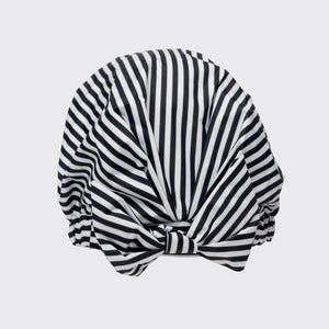 The KITSCH - LUXURY SHOWER CAP, with chic black and white stripes, is elegantly showcased in a pink box. The packaging highlights its waterproof, no-slip grip features and charming illustrations, complemented by a model's photo demonstrating its beauty.
