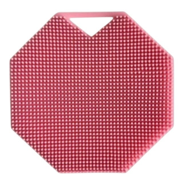 A rose-colored, octagonal SILICONE BODY AND EXFOLIATION BRUSH by SMILE BOUTIQUES, featuring raised dots for gentle exfoliation, rests on a white surface. Brown paper packing material is scattered to the right of the brush.