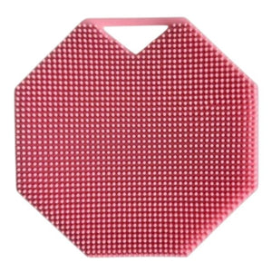 A rose-colored, octagonal SILICONE BODY AND EXFOLIATION BRUSH by SMILE BOUTIQUES, featuring raised dots for gentle exfoliation, rests on a white surface. Brown paper packing material is scattered to the right of the brush.