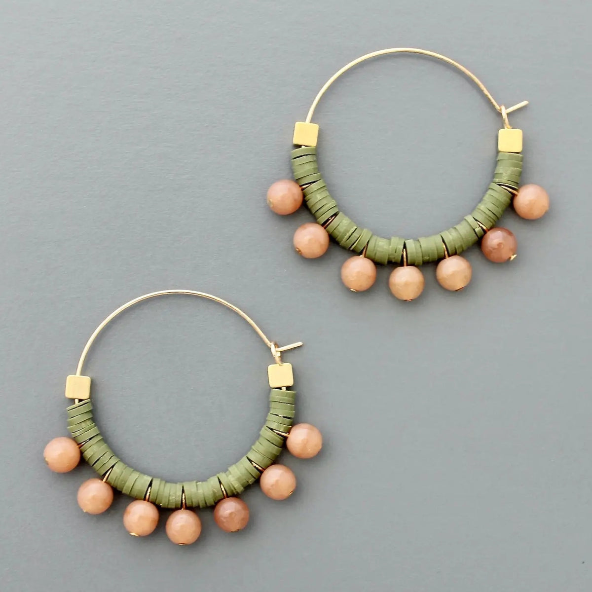 The DAVID AUBREY - GREEN AND PEACH HOOP EARRINGS by DAVID AUBREY feature gold plated hoops adorned with green polymer discs and round peach beads hanging along the bottom, shown against a flat gray background.