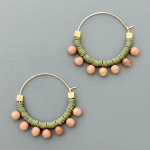 The DAVID AUBREY - GREEN AND PEACH HOOP EARRINGS by DAVID AUBREY feature gold plated hoops adorned with green polymer discs and round peach beads hanging along the bottom, shown against a flat gray background.