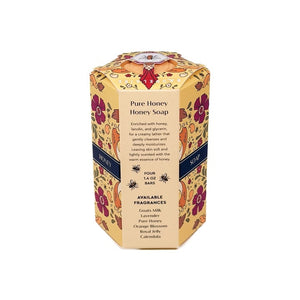 BAUDELAIRE Pure Honey Soap 1.4 oz Quartet, featuring a hexagonal honeycomb pattern and a bee emblem, is displayed with its coordinating floral packaging on a white surface alongside a honey dipper, soap bar, and natural bath sponge. Both the triple-milled BAUDELAIRE soap and box are adorned with the bee motif.