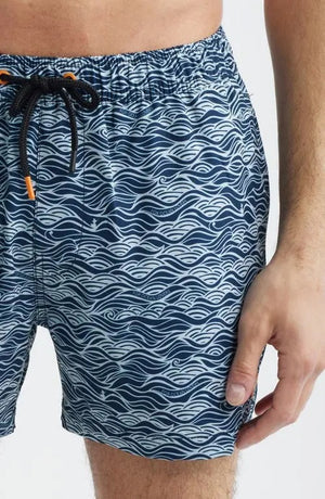 A shirtless man stands with hands in his pockets against a plain light background, modeling SAVE THE DUCK's Ademir Swim Trunks in Ondine Off White on Blue, crafted from quick-dry recycled polyester.