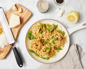 A small glass jar of JACOBSEN SALT CO. JACOBSEN SALT - INFUSED BLACK PEPPER SALT with a white lid rests on a light beige surface against a light gray background. The dark label with white text highlights this floral, spicy blend.