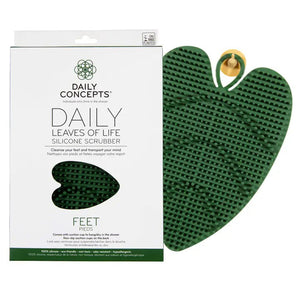 Packaging for DAILY CONCEPTS LEAVES OF LIFE FOOT SCRUBBER. The green, leaf-shaped scrubber is depicted next to the packaging, which emphasizes its purpose for foot care and its ability to cleanse and relax your mind, enriching your shower experience. The packaging predominantly features a white background with green accents.