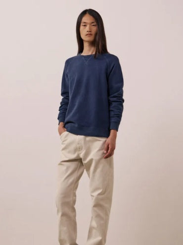 A person with long, straight hair is wearing the HARTFORD - LIGHT FLEECE SWEATSHIRT IN NAVY by HARTFORD and light-colored pants, standing with one hand in their pocket against a plain white background.