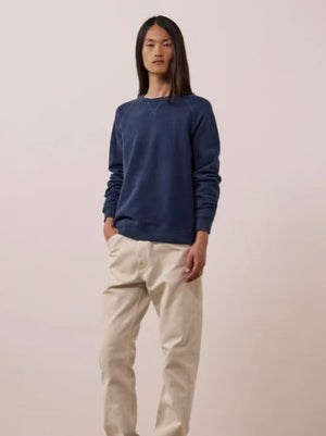 A person with long, straight hair is wearing the HARTFORD - LIGHT FLEECE SWEATSHIRT IN NAVY by HARTFORD and light-colored pants, standing with one hand in their pocket against a plain white background.