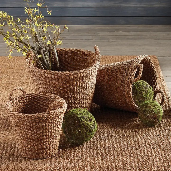 The NAPA HOME AND GARDEN Seagrass Tapered Basket with Handles and Cuff, Large, is shown from above, highlighting its natural seagrass texture and expert craftsmanship on a matching surface.