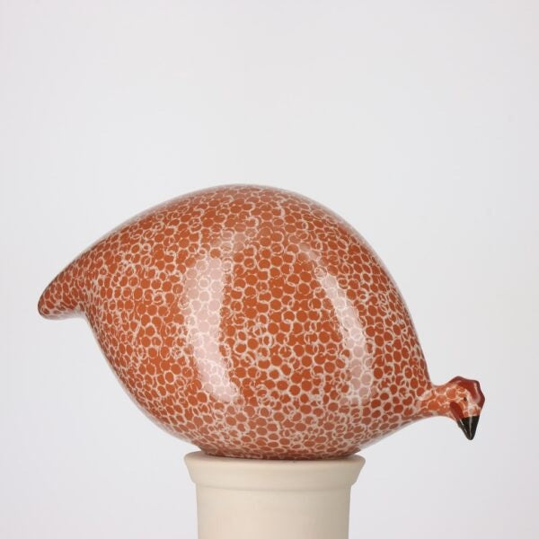 The LES CERAMIQUES DE LUSSAN - PECKING CERAMIC GUINEA IN RED SPOTTED WHITE features a handcrafted French guinea hen with a rounded form, adorned in a red and white spotted pattern. Perched atop a simple, light-hued cylindrical base, this ceramic accent from LES CERAMIQUES DE LUSSAN channels the classic charm of Heidi Caillard designs, imparting whimsical character to any decor.