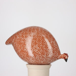 The LES CERAMIQUES DE LUSSAN - PECKING CERAMIC GUINEA IN RED SPOTTED WHITE features a handcrafted French guinea hen with a rounded form, adorned in a red and white spotted pattern. Perched atop a simple, light-hued cylindrical base, this ceramic accent from LES CERAMIQUES DE LUSSAN channels the classic charm of Heidi Caillard designs, imparting whimsical character to any decor.