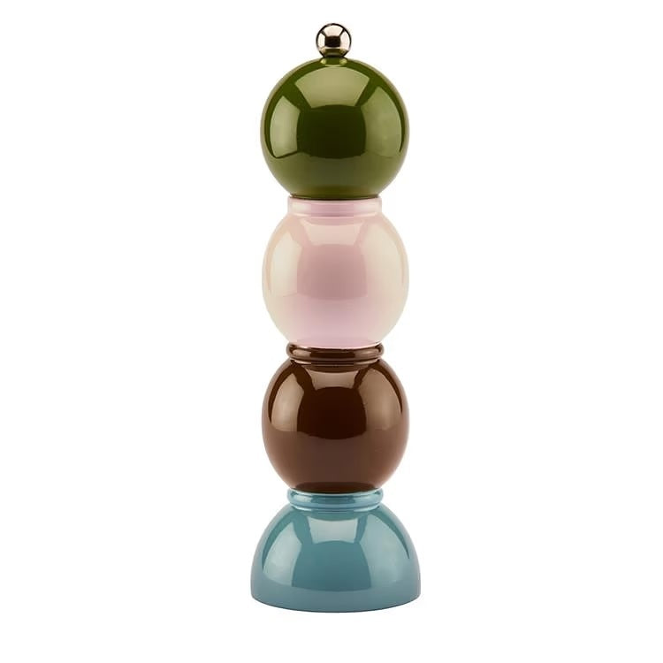 Three vibrant ADDISON ROSS LONDON Bobbin Salt or Pepper Mills (24cm) from ADDISON ROSS are stacked on a kitchen counter near wooden cabinets, with jars of dry food visible in the background.