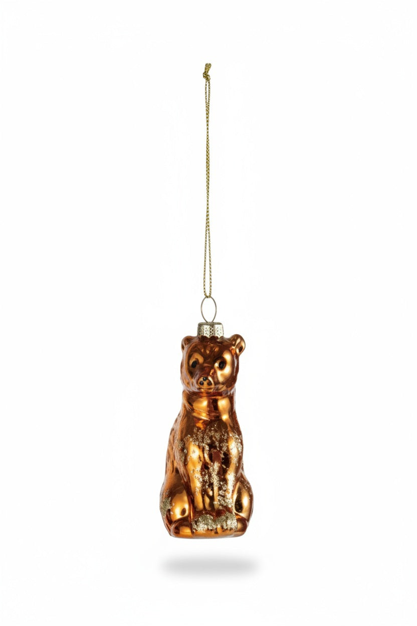 A metallic gold mercury glass BEAR ORNAMENT WITH GLITTER sits on a small pile of green glitter atop a stack of old books.