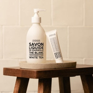 A white tube of COMPAGNIE DE PROVENCE - TRAVEL HAND CREAM WHITE TEA 1OZ from CIE LUXE BRANDS, labeled “Creme Mains Hydratante The Blanc” in black text on a plain white background; this luxurious hand cream is enriched with nourishing ingredients and made in Italy.