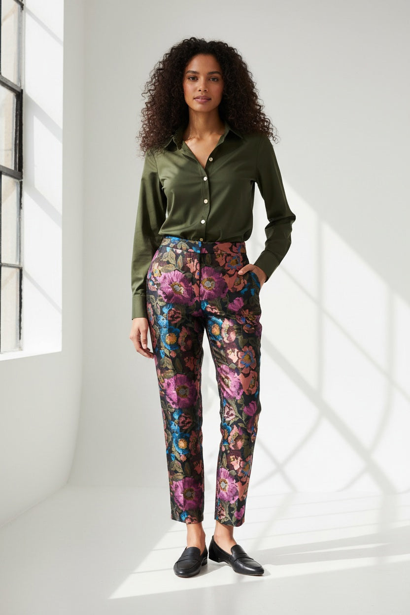 A person wears the HINSON WU Jolene Jacquard Pant in Floral Bouquet—high-waisted, ankle-length tailored trousers featuring a vibrant floral pattern in pink, purple, blue, and orange—paired with a dark green shirt and light pink heels.