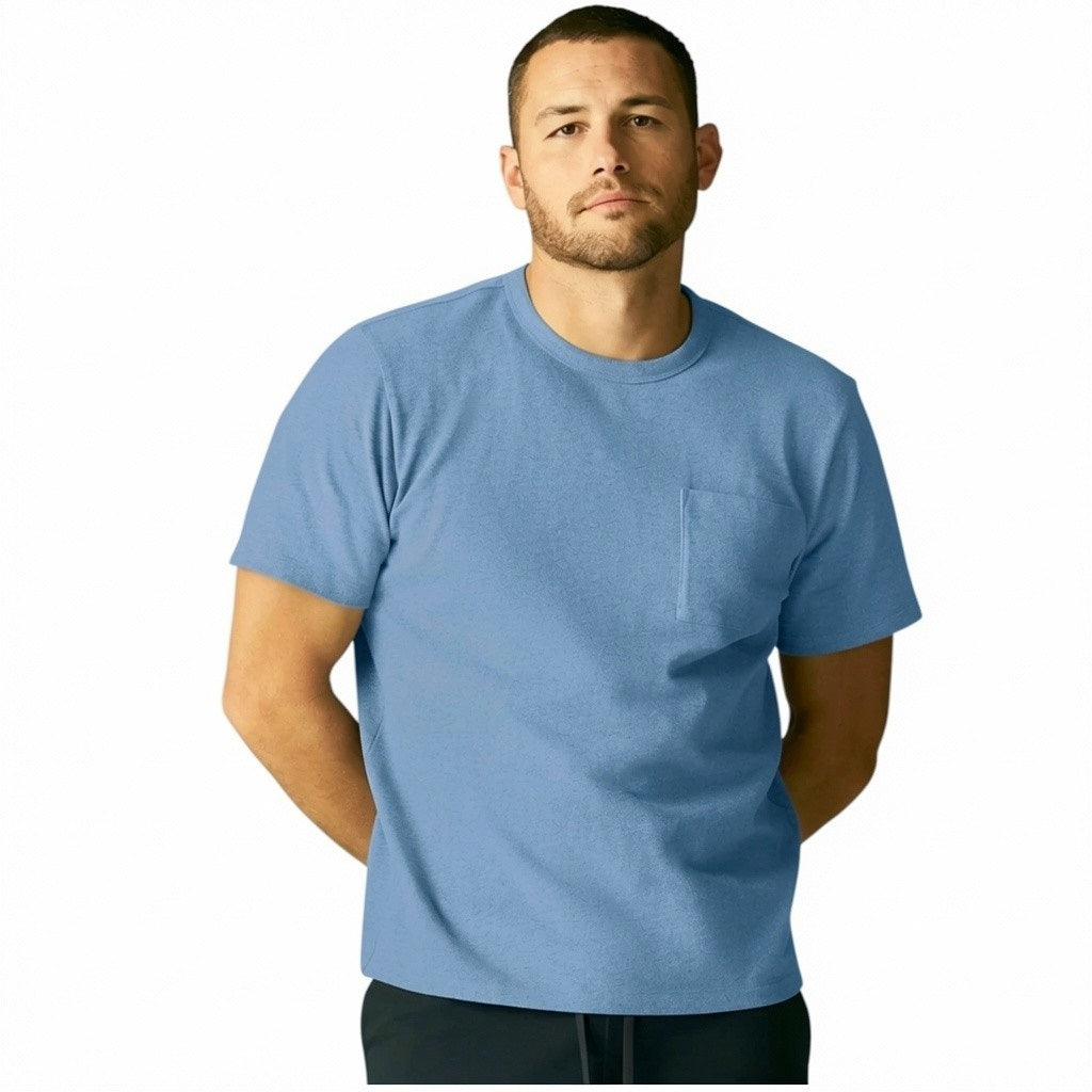 A man with short curly hair wears the MACK WELDON Heavyweight Slub Cotton Pocket T-Shirt in Dean Blue with dark pants, standing against a plain white background.