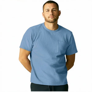 A man with short curly hair wears the MACK WELDON Heavyweight Slub Cotton Pocket T-Shirt in Dean Blue with dark pants, standing against a plain white background.