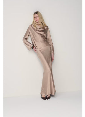 A person wearing the MILVA MI - LONG SATIN SKIRT IN SAND by MILVA, paired with pointed black shoes and standing against a plain, light background.