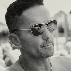 The CADDIS HOOPER Sunglasses feature a gold metal aviator-style frame, dark green polarized lenses, double bridge, black temple tips, and lightweight design, shown from the front against a white background.