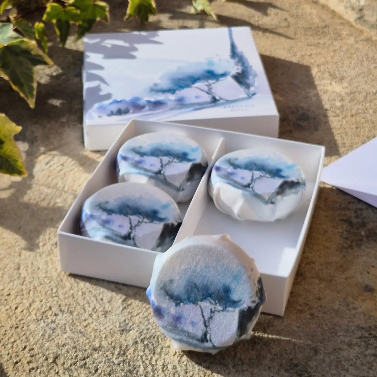 Four round, creamy white L&#39;AUGUSTE PROVENCE artisanal lavender soaps are elegantly boxed—a beautiful Provence gift by L&#39;AUGUSTE PROVENCE, ready to delight any recipient.