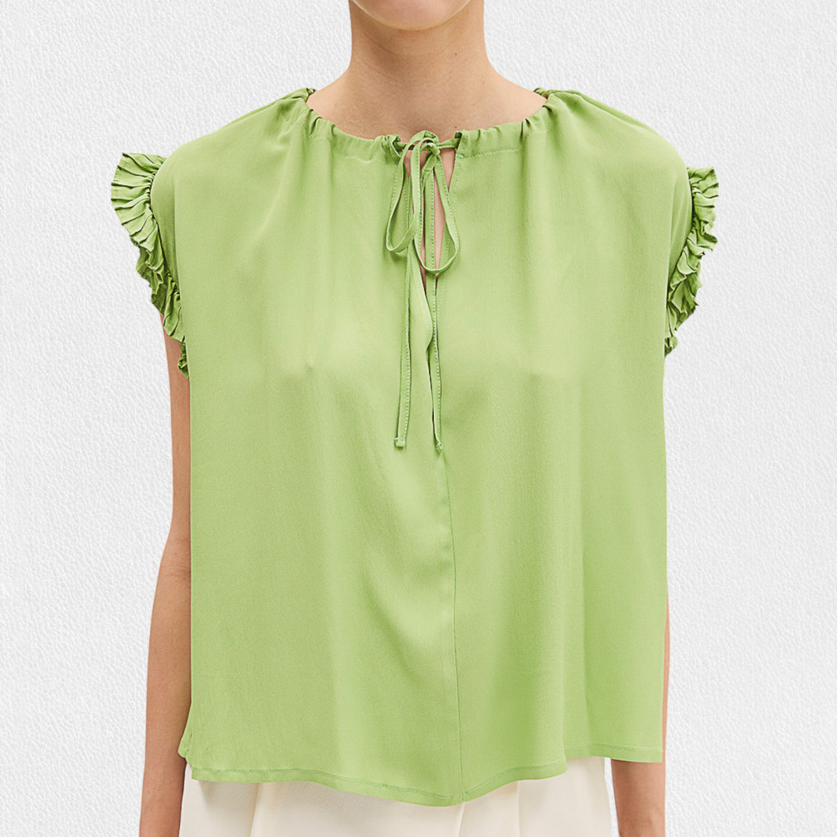 A woman wears the MEIMEIJ Cap Sleeve Blouse, a light green viscose top with ruffle cap sleeves and a tied neckline from MEIMEIJ, paired with white bottoms against a plain light background.