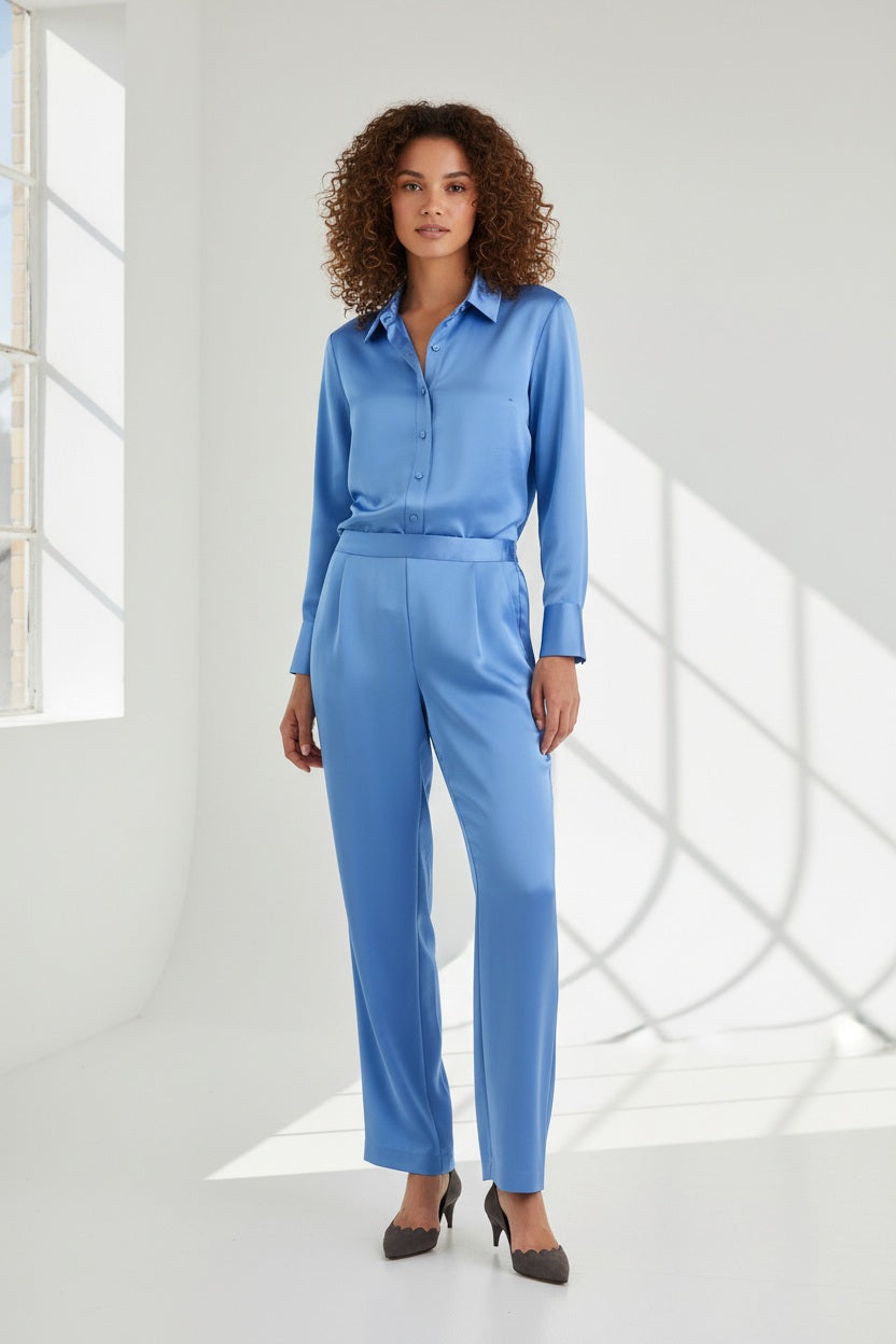 Model wears the HINSON WU - HOSTESS LIQUID SATIN PANT IN SKY BLUE by HINSON WU, featuring a relaxed straight leg and elastic waistband in luminous, light-catching sky blue satin. Styled with the matching long-sleeve top, they are pictured from the back against a neutral backdrop and complete the look with gray pointed-toe shoes.