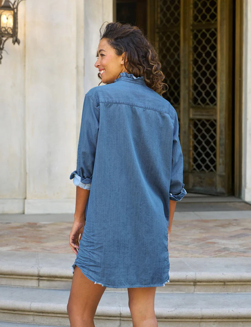 The FRANK &amp; EILEEN Mary Ruffle Shirtdress in vintage stone-washed indigo features long sleeves rolled up to the elbows, a ruffle collar, and a front button-down design with a chest pocket. A slightly frayed hem adds charm against the plain white background.