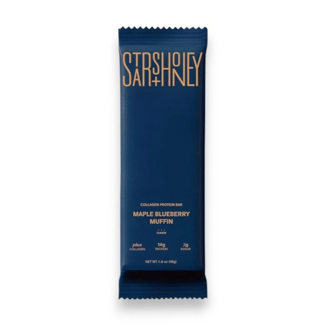 A blue wrapper labeled “STARS+HONEY - MAPLE BLUEBERRY MUFFIN”—a tasty collagen protein bar blending maple and blueberry flavors from the brand STARS+HONEY—rests on a beige surface, with nutritional information visible.