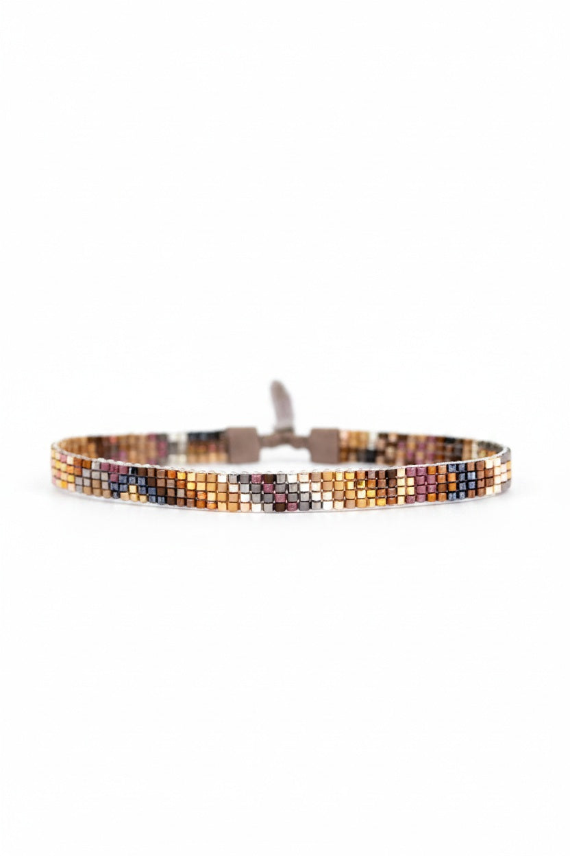 The JULIE ROFMAN - ORO BRACELET by JULIE ROFMAN JEWELRY features a handwoven design with small, vibrant square beads in shades of orange, yellow, pink, and black. This stylish bracelet is finished with a loop closure on a white background.