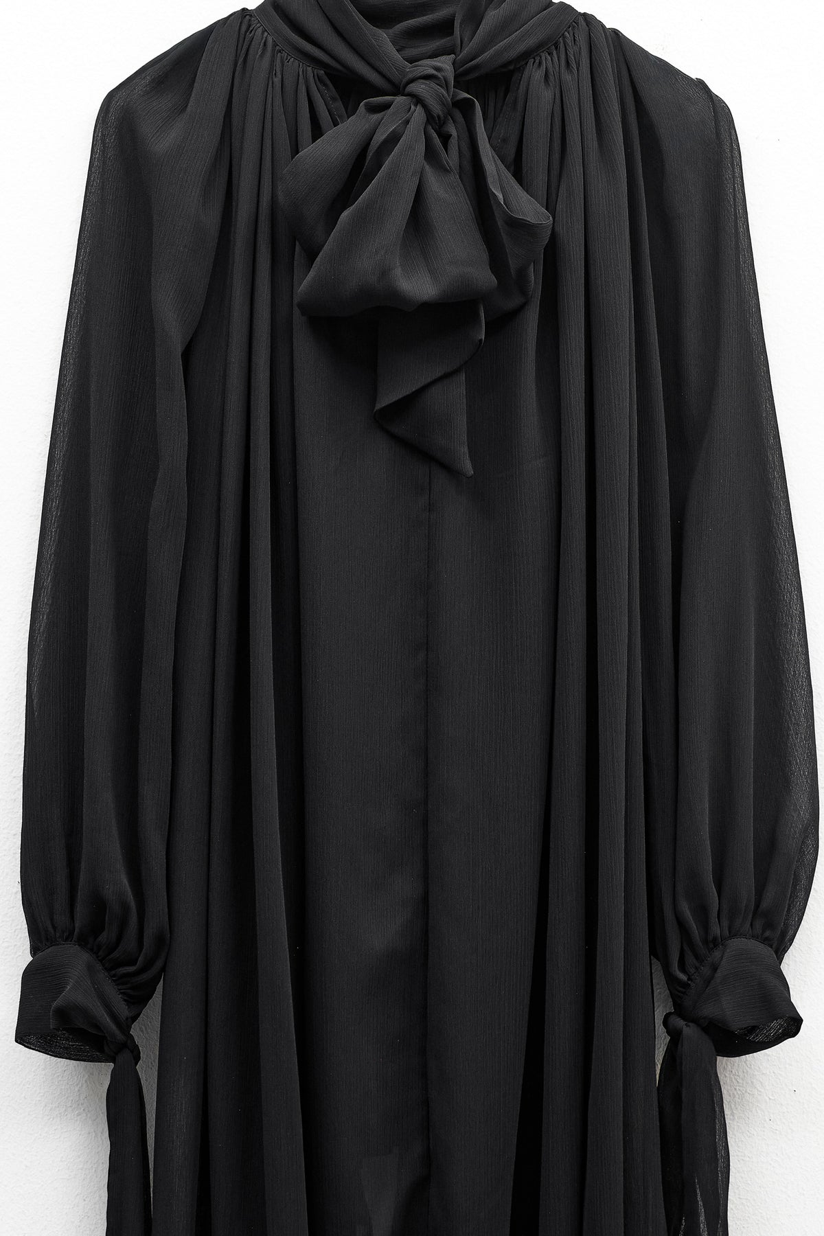 The ELEH - THE CHIFFON TIE NECK TOP by ELEH is a sheer black chiffon blouse with long sleeves, a high neckline, and an oversized bow tie at the collar—an elegant evening statement inspired by classic blouses.