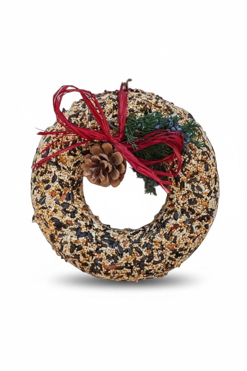 A MR BIRD - WILDFEAST WREATH made of various birdseeds, decorated with a pinecone, a sprig of greenery, and a red ribbon bow.