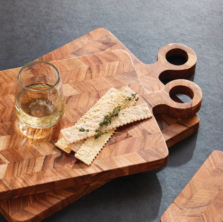 Two NAPA HOME AND GARDEN RENATA Serving Boards, featuring chevron patterns and handles, are stacked to display their natural acacia wood grain against a white background.