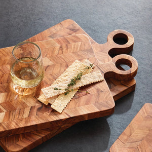 Two NAPA HOME AND GARDEN RENATA Serving Boards, featuring chevron patterns and handles, are stacked to display their natural acacia wood grain against a white background.