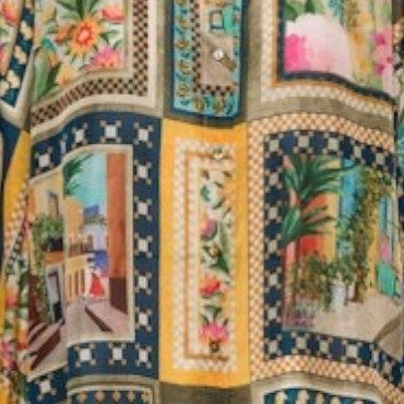 The MOMONI - ASPEN PANT features a luxurious haboutai silk fabric with a geometric pattern of squares and rectangles, adorned with vibrant floral motifs and architectural designs in colors like yellow, green, and blue.