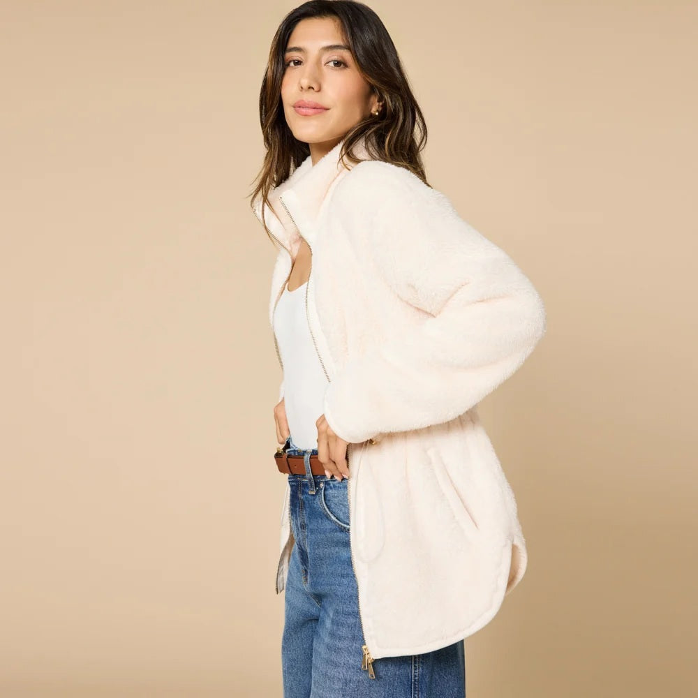 A woman wearing a cream SOFTIES - DREAMPLUSH DOUBLE ZIP JACKET / TUNIC with a cinched waist, paired with wide-leg denim culottes for cozy velvety softness.