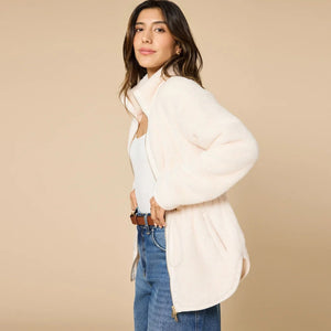 A woman wearing a cream SOFTIES - DREAMPLUSH DOUBLE ZIP JACKET / TUNIC with a cinched waist, paired with wide-leg denim culottes for cozy velvety softness.