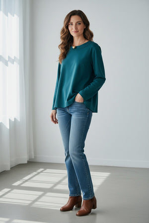 A woman with straight dark hair wears the MEIMEIJ Long Sleeve Ponte Swing Top in teal and a gold pendant necklace, standing against a plain light background, facing forward with a neutral expression.