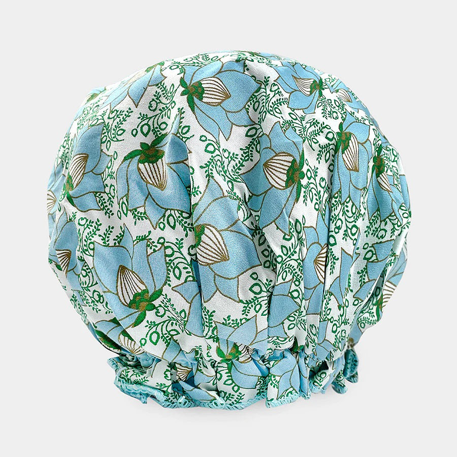 The BATH ACCESSORIES COMPANY offers the BOUFFANT SHOWER CAP, featuring a blue floral and green leaf pattern on a light base. It includes waterproof inner-layers and gathered edges for a puffy, rounded shape.