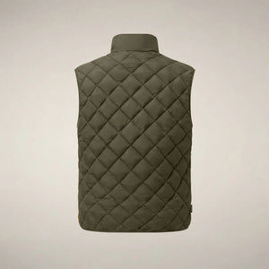 A person stands facing forward, wearing the SAVE THE DUCK - FABRICE Puffer Vest in Snake Green with Plumtech® padding over a beige sweater, paired with white pants and tan shoes, against a plain light background.