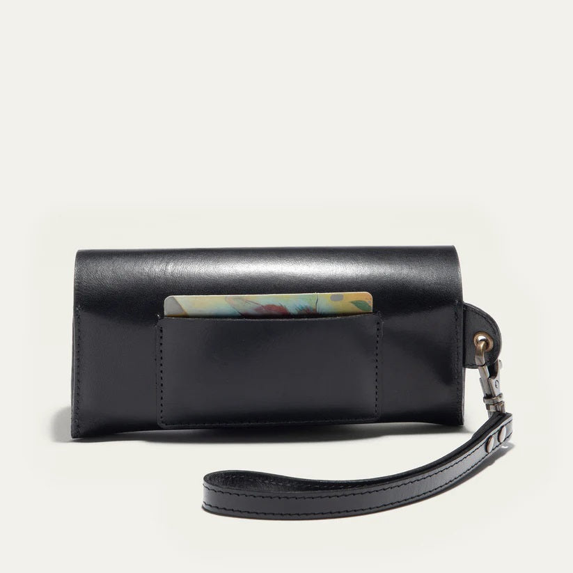 The WILL LEATHER GOODS - EYEGLASS CASE IN BLACK is a handcrafted Italian leather case with a flap closure, embossed logo on the front, and an attached wrist strap on the left, shown against a plain light background.