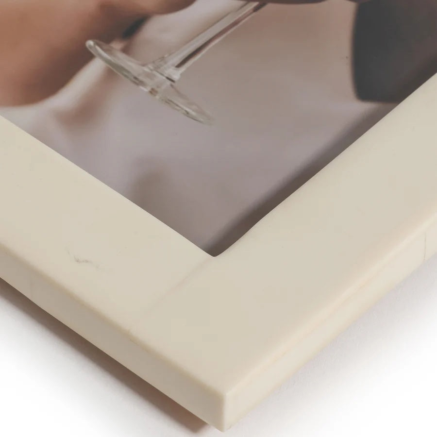 Two luxury ZODAX photo frames—one crafted from natural white horn inlay and the other an elegant ivory resin—display portraits: one shows a person holding a glass, while the other features a close-up of a face with a finger touching the lips. Both WHITE HORN AND IVORY RESIN FRAME - 5X7 rest on a patterned surface.