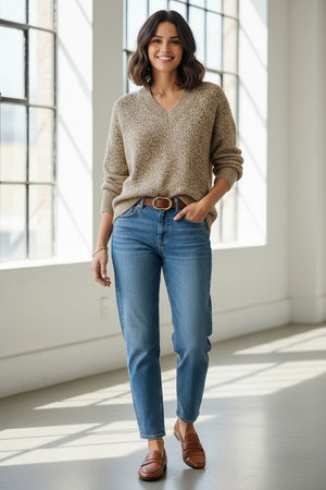 A person wearing the KINROSS CASHMERE Sequin Marle Easy Vee Neck Sweater in Scotch, paired with blue jeans and a brown belt, stands with hands in their pockets against a plain light background.