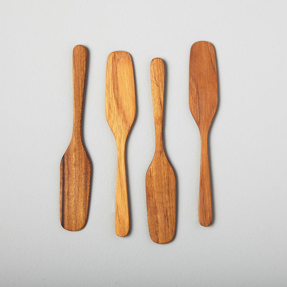 The BE HOME - TEAK OAR SPREADER set by BE HOME, INC includes four sustainably sourced teak wood spreaders with smooth, rounded handles and paddle-shaped blades, displayed side by side on a light gray background.