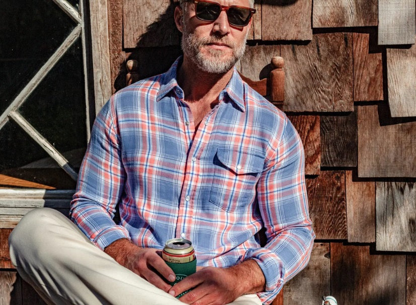 Close-up of a person's chest in the CRIQUET - DOUBLE CLOTH FLANNEL PEARL SNAP SHIRT IN SUNSET, a blue, white, and orange plaid flannel with pearl snaps, front pocket with flap, and visible chest hair at the open collar.